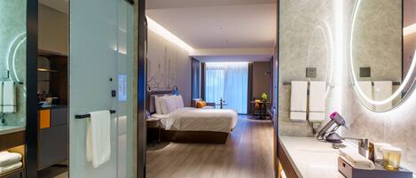 A modern hotel room with a large bed, a separate bathroom with a vanity, and a view of the cityscape through the window.