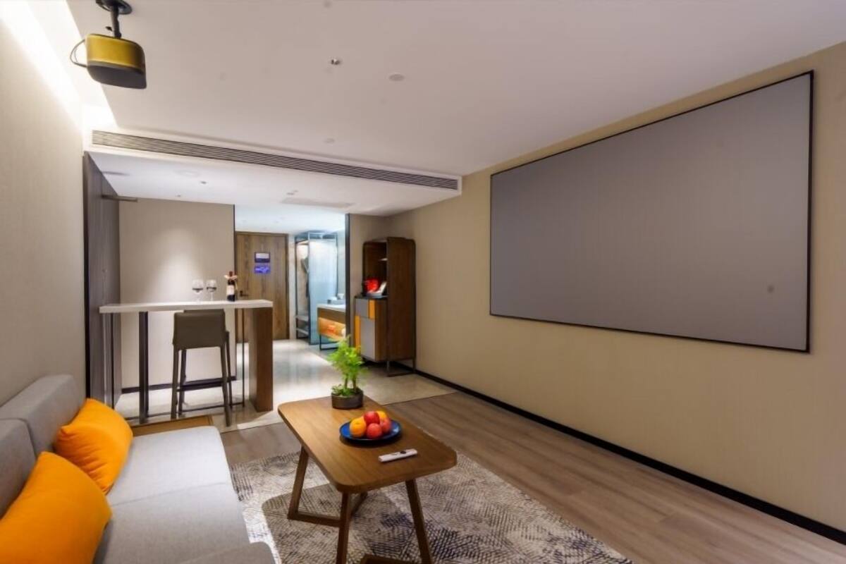 A modern living room with a sofa, a coffee table with fruit, a TV, and a kitchen area in the background.