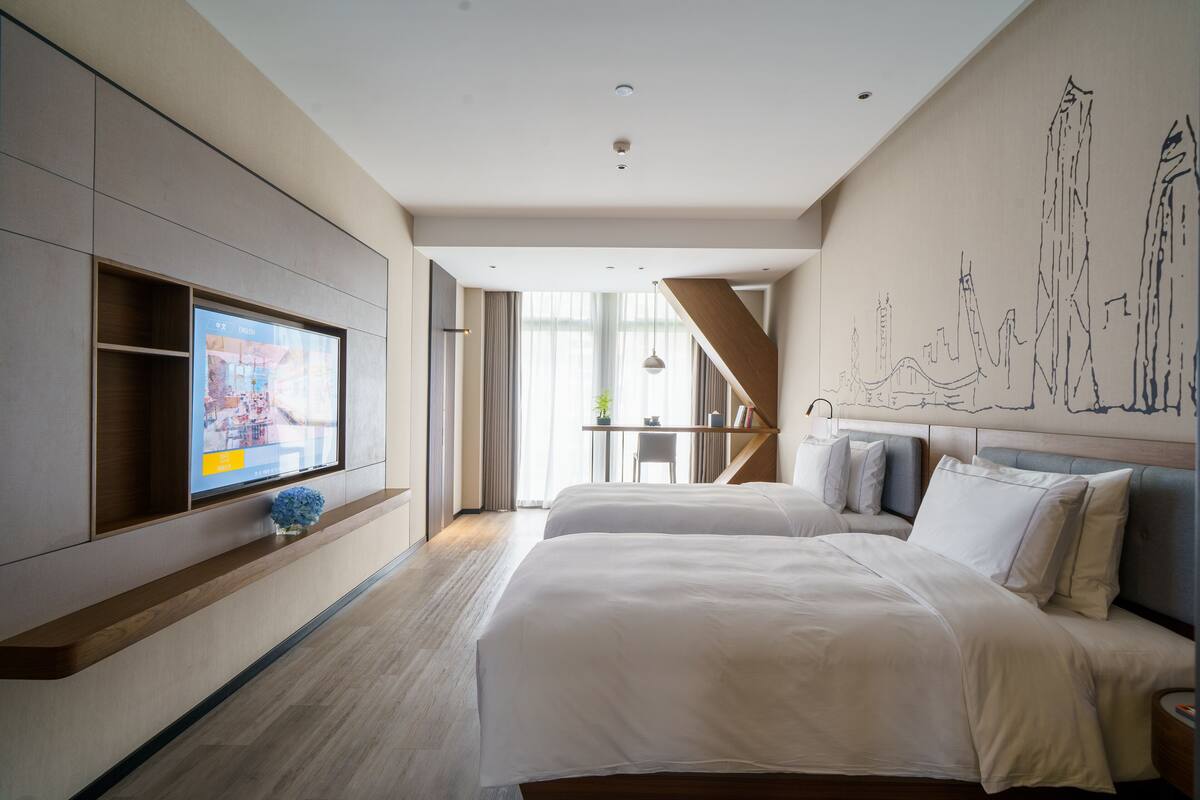 A modern hotel room with a large bed, a TV mounted on the wall, and a staircase leading to an outdoor area.