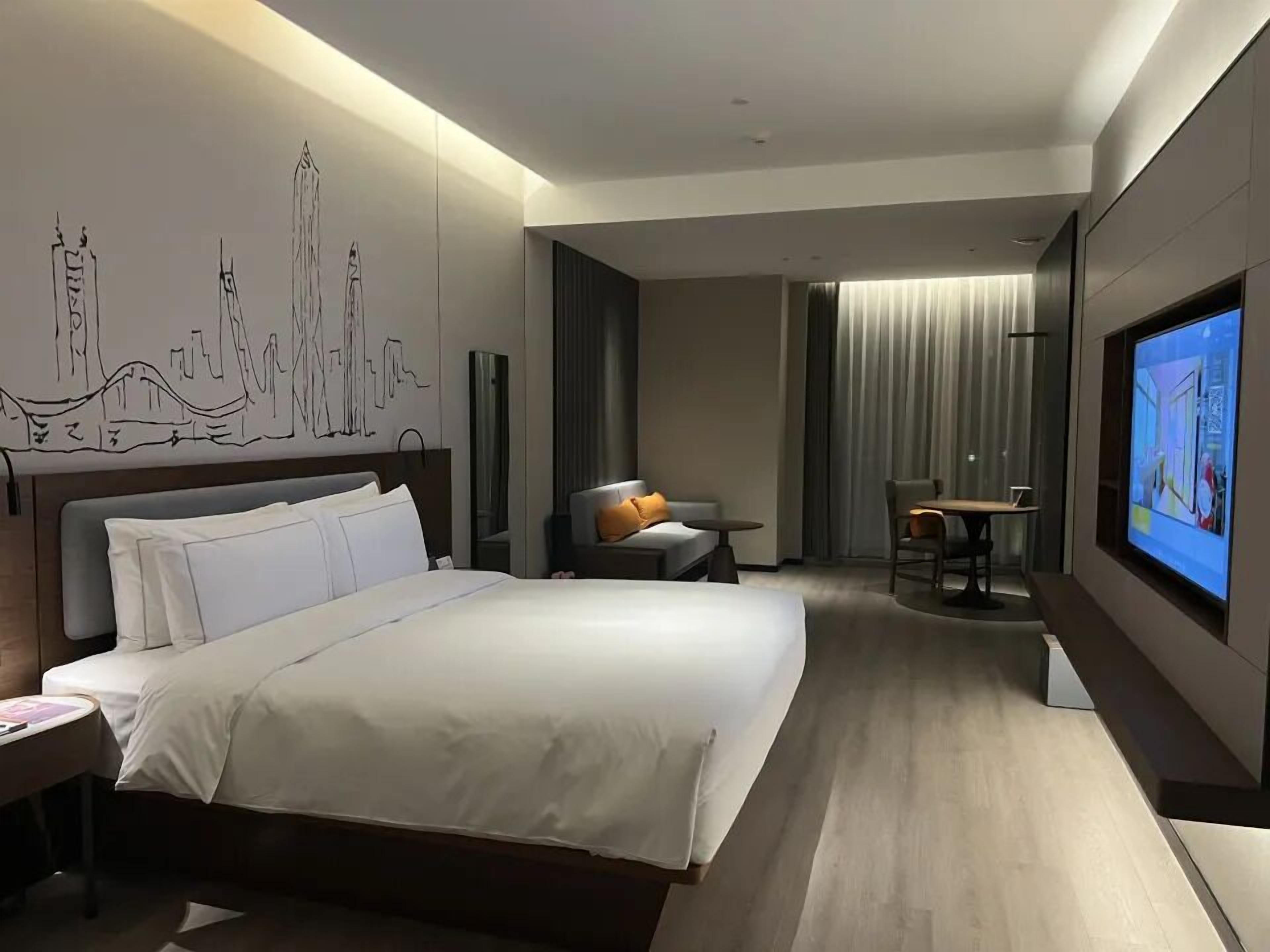 A modern hotel room with a large bed, a desk, and a television.