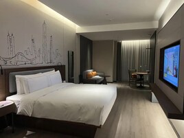 A modern hotel room with a large bed, a desk, and a television.