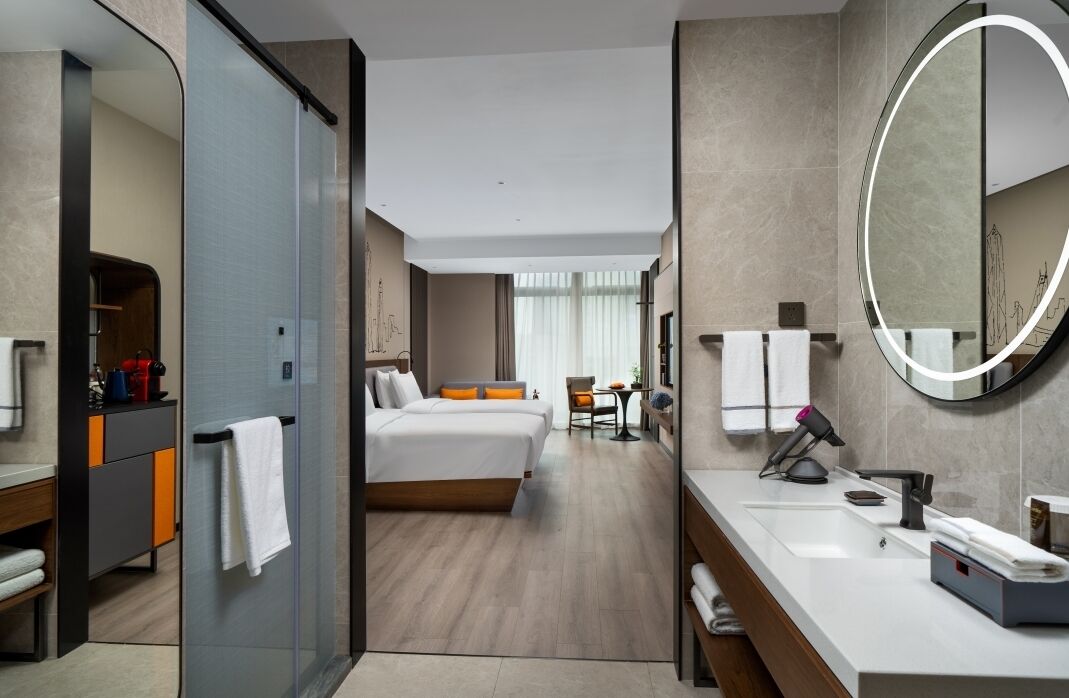 A hotel room with a bed, a bathroom with a mirror, and a desk with a chair.