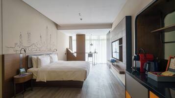 A modern hotel room with a large bed, a desk with a coffee machine, and a cityscape mural on the wall.