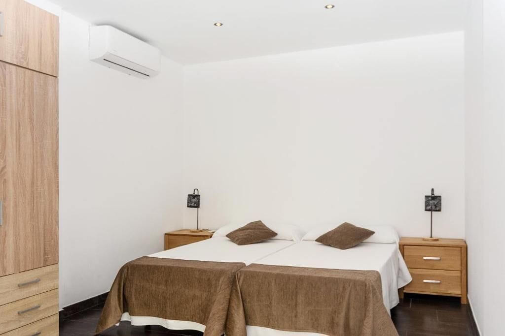 Ein Schlafzimmer mit einem Bett, zwei Nachttischen, einem Kleiderschrank und einer Klimaanlage.