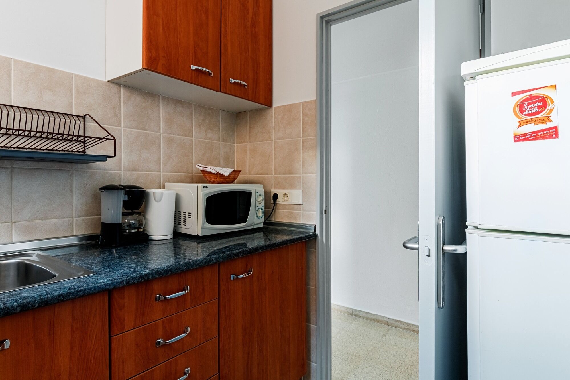 Eine Küche mit Holzausstattung, einer Mikrowelle, einer Kaffeemaschine und einem Kühlschrank.
