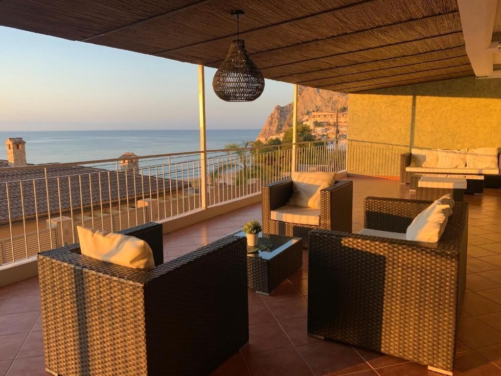 Un balcon agrémenté de meubles en osier, d’un luminaire suspendu et offrant une vue sur la mer.