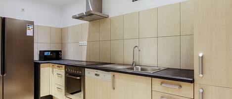 Une cuisine moderne avec des meubles de couleur bois clair, un évier en acier inoxydable et un four encastré.