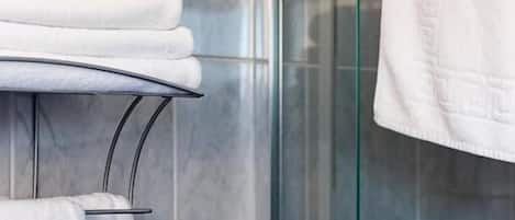 Une salle de bain dotée d’une douche à parois de verre, d’un porte-serviettes avec des serviettes pliées et d’un mur recouvert de carreaux décoratifs.