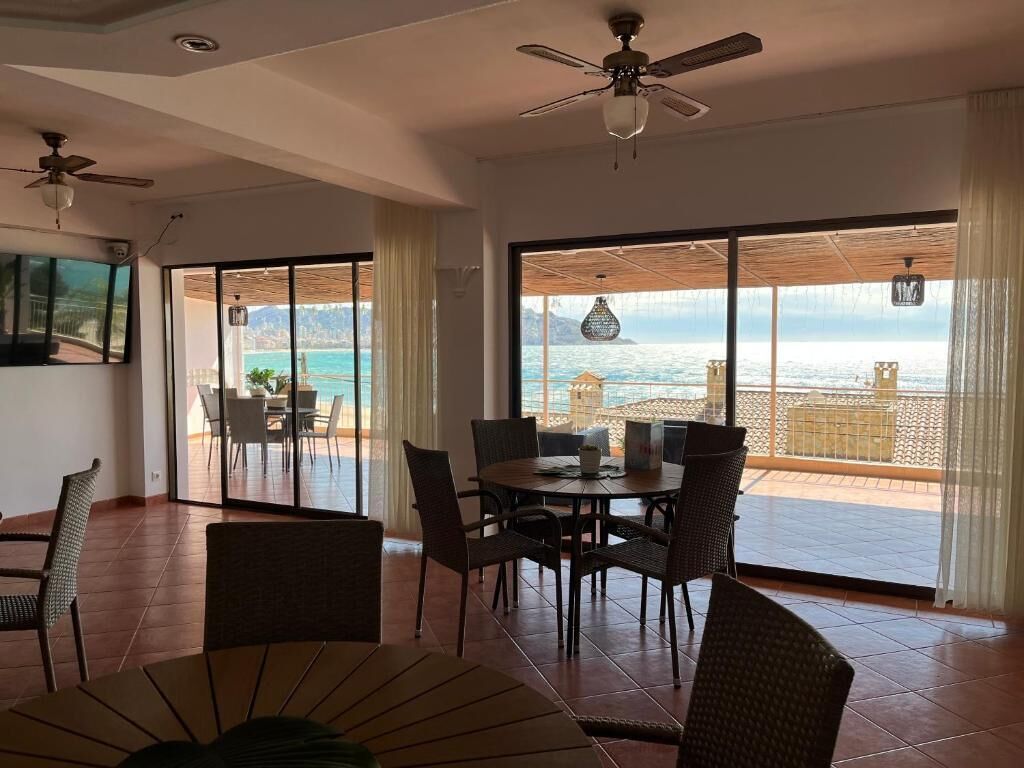 A spacious room with a large dining table and chairs, a ceiling fan, and a view of the ocean through large sliding glass doors.