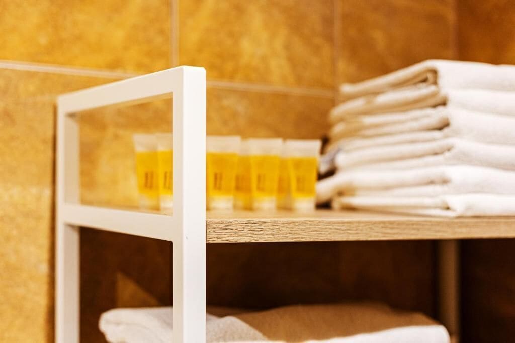 A bathroom with a shelf holding folded towels and a glass of yellow liquid.