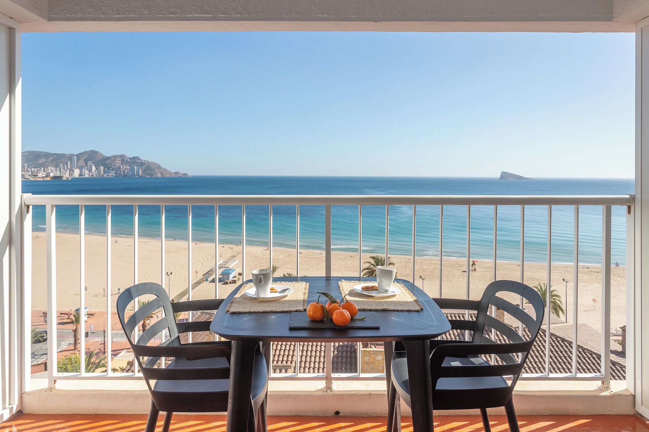 A balcony with a table and chairs overlooking a beach.