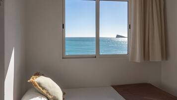 A room with a bed, a window with a view of the sea, and a curtain.