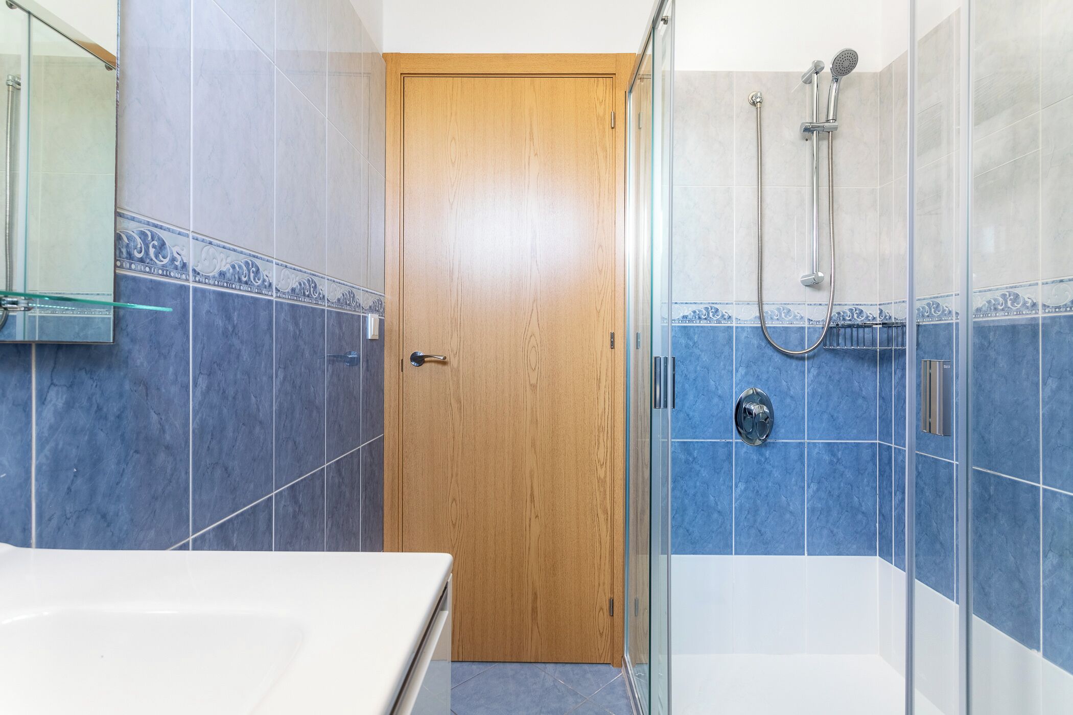 A bathroom with a wooden door, a glass shower enclosure, and blue-tiled walls.