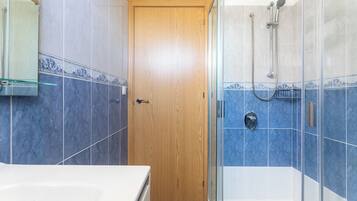 A bathroom with a wooden door, a glass shower enclosure, and blue-tiled walls.