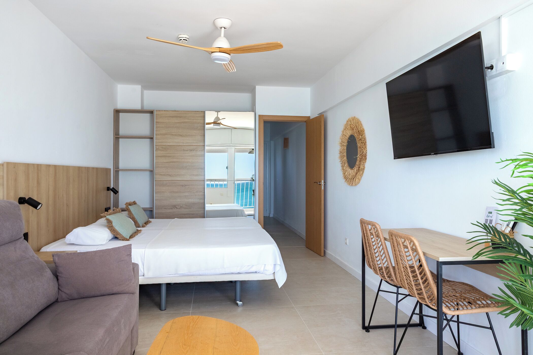 Ein modernes Hotelzimmer mit Bett, Sofa, Schreibtisch mit Stühlen, Fernseher und Deckenventilator, mit Blick ins Freie.