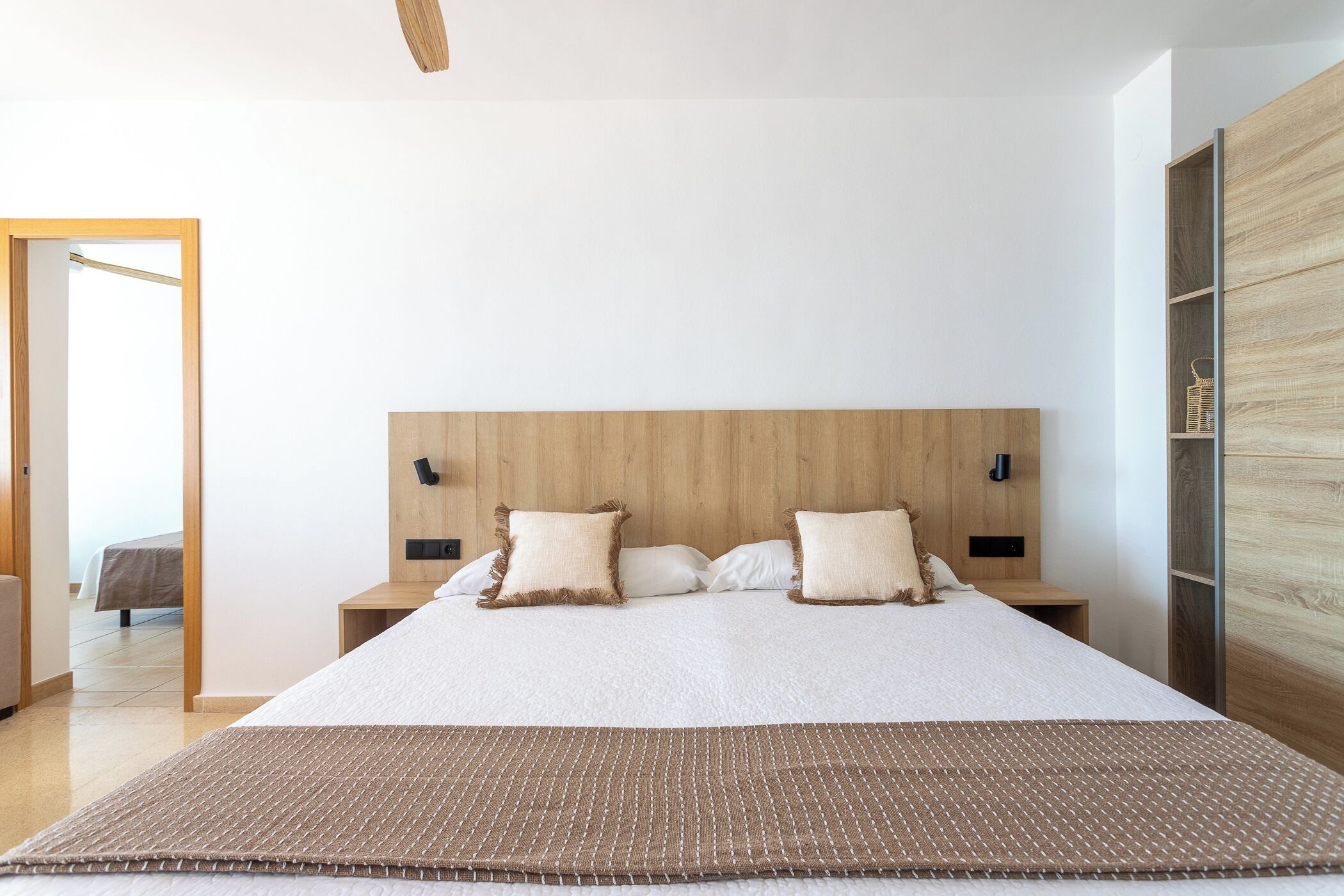 A modern bedroom with a large bed, wooden headboard, bedside tables, and a wooden wardrobe.