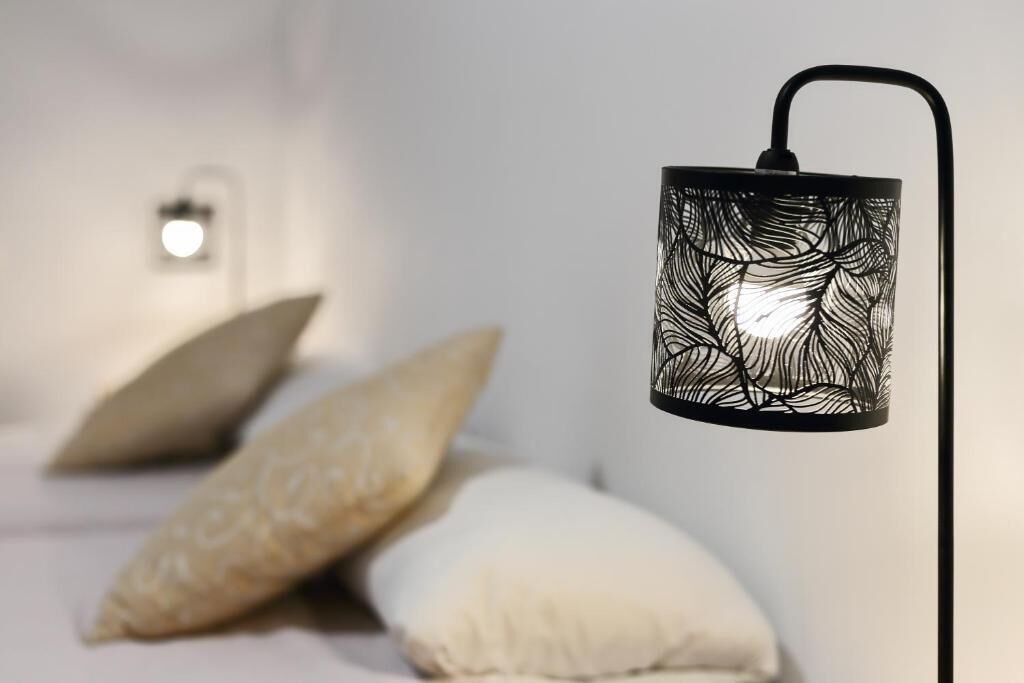 A modern bedroom with a hanging black metal lamp, a bedside table, and two pillows.