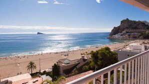A coastal view from a balcony overlooking a beach with a rocky cliff and buildings in the background. - Apartamentos Mirador  (Benidorm)
