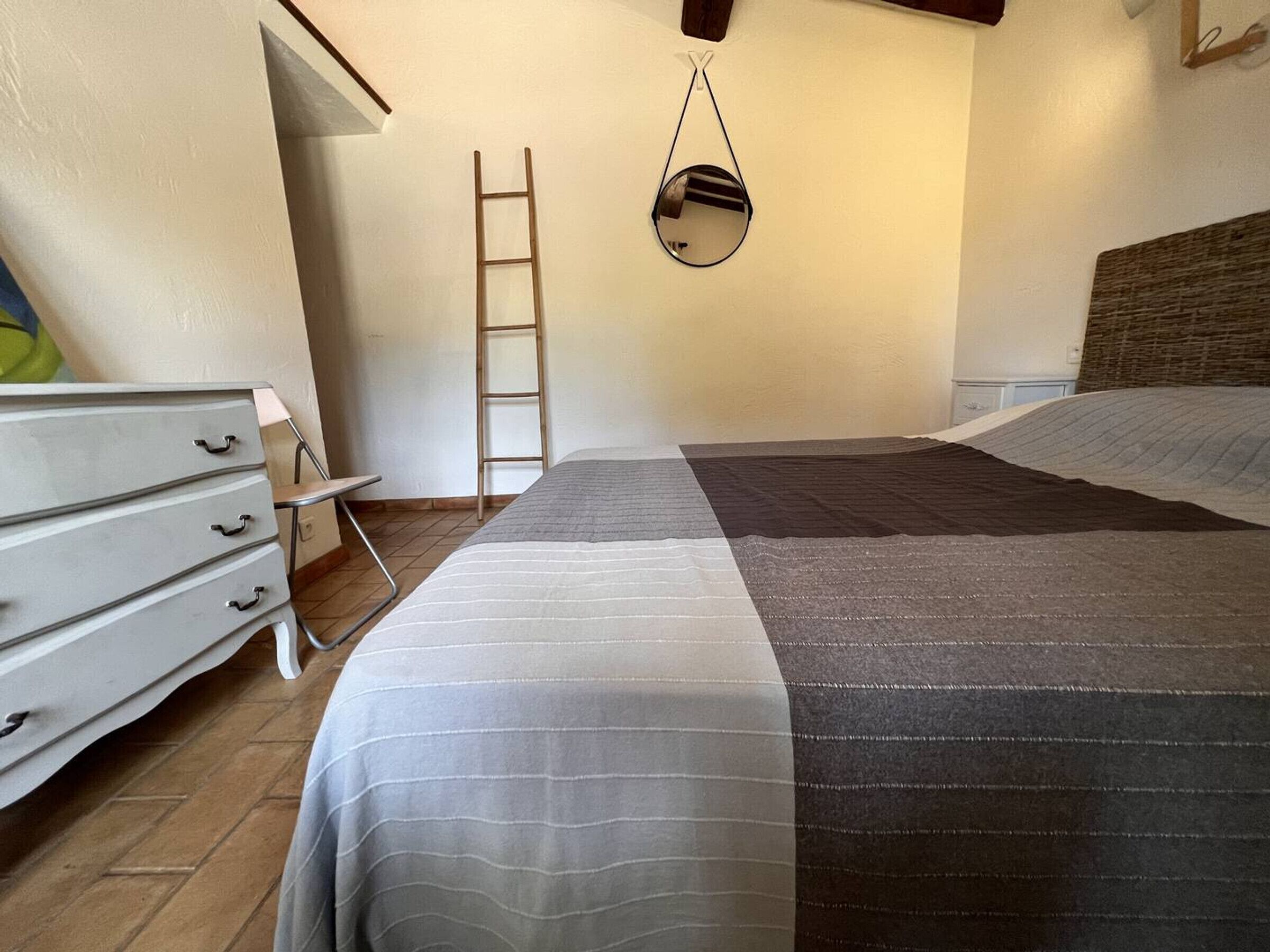 A bedroom with a bed, a dresser, a ladder, and a hanging mirror.