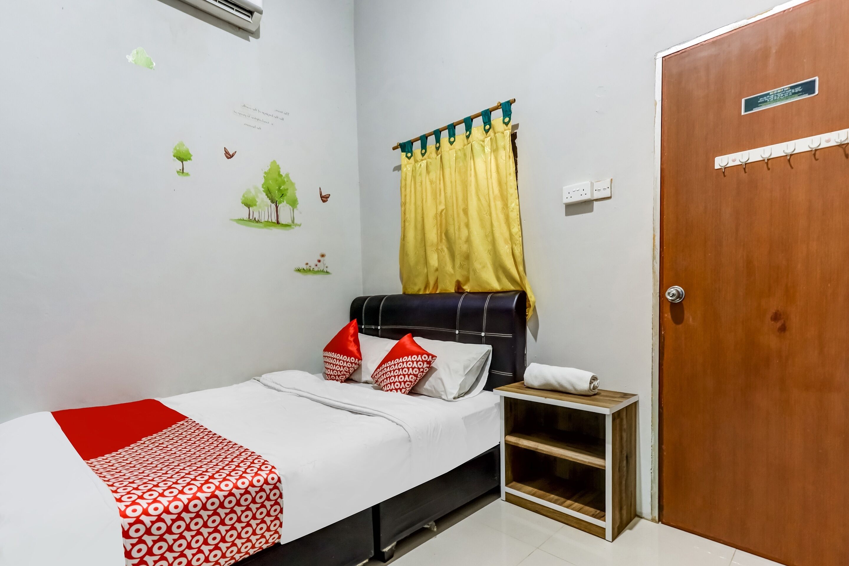 A neatly arranged bedroom with a bed, a bedside table, a wooden nightstand, a door, and a window with a curtain.