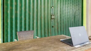 Une table en bois, sur laquelle se trouvent un ordinateur portable et des documents, adossée à un mur en métal ondulé vert.