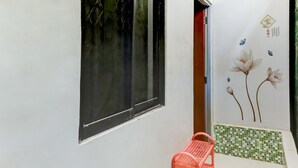 Un couloir étroit avec une fenêtre, une chaise rouge et un mur décoratif orné de motifs floraux.