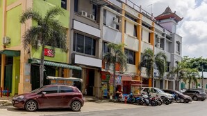 Un immeuble à plusieurs étages, avec divers commerces au rez-de-chaussée, des voitures et des motos garées le long de la rue.