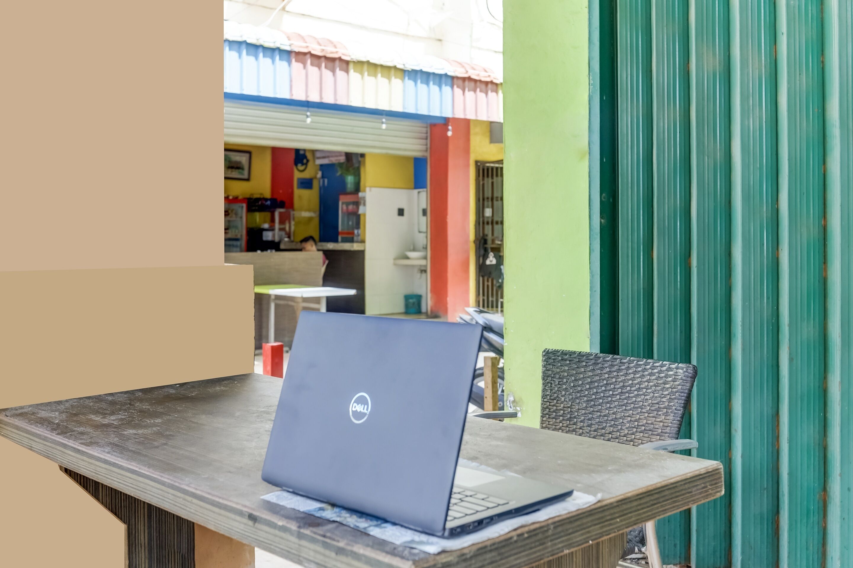 A laptop on a table with a chair, a green wall, and a colorful interior in the background.