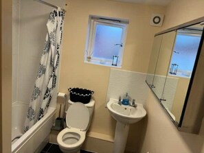 Bathroom features a toilet, sink, and bathtub with a window and mirror.