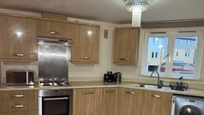 A modern kitchen with wooden cabinets, stainless steel appliances, a built-in oven, a microwave, a sink, and a washing machine. - Flat In Willen - Milton Keynes suitable for contractors and family staycations  (Milton Keynes)
