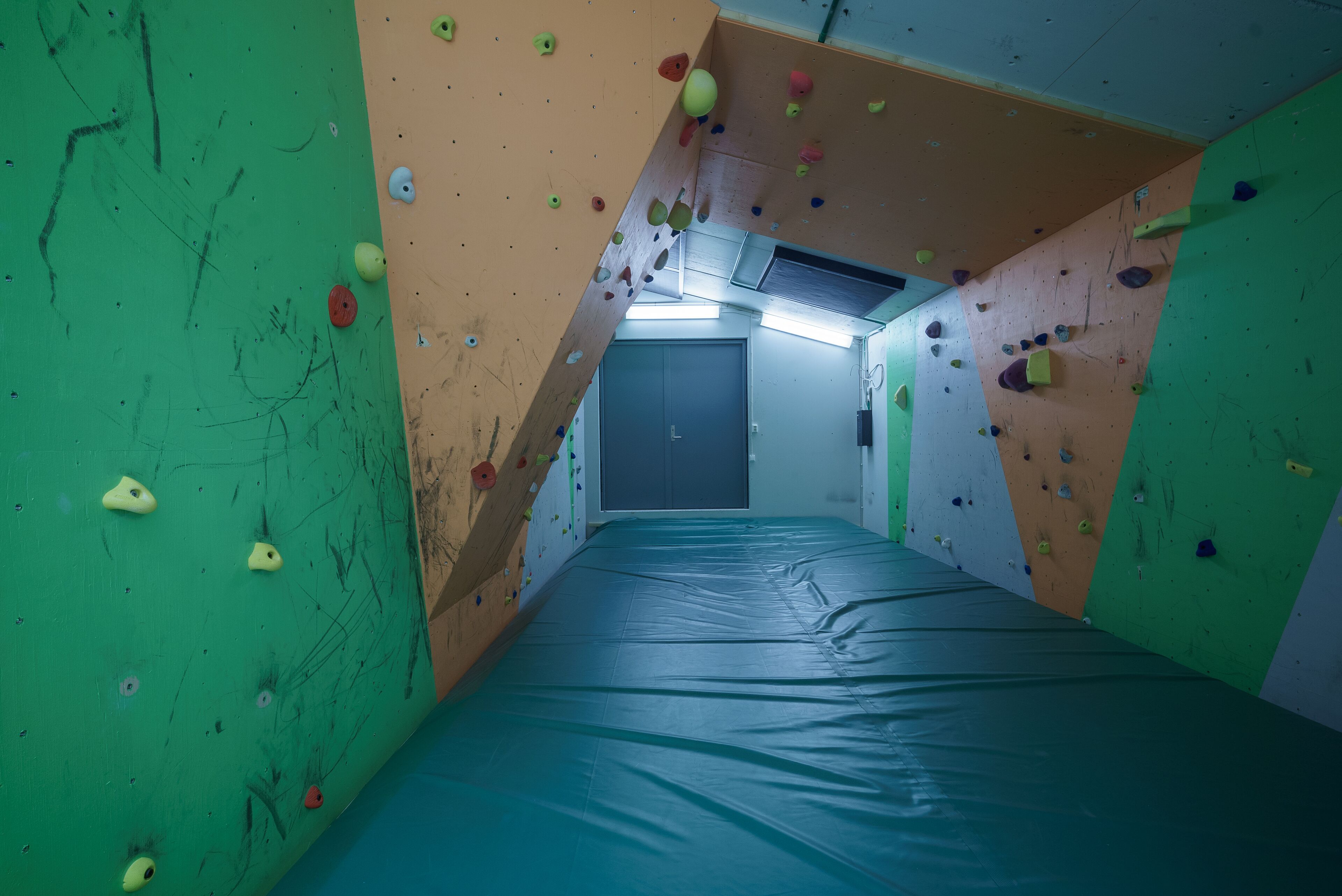 A climbing gym with padded flooring, climbing walls, and a door in the background.