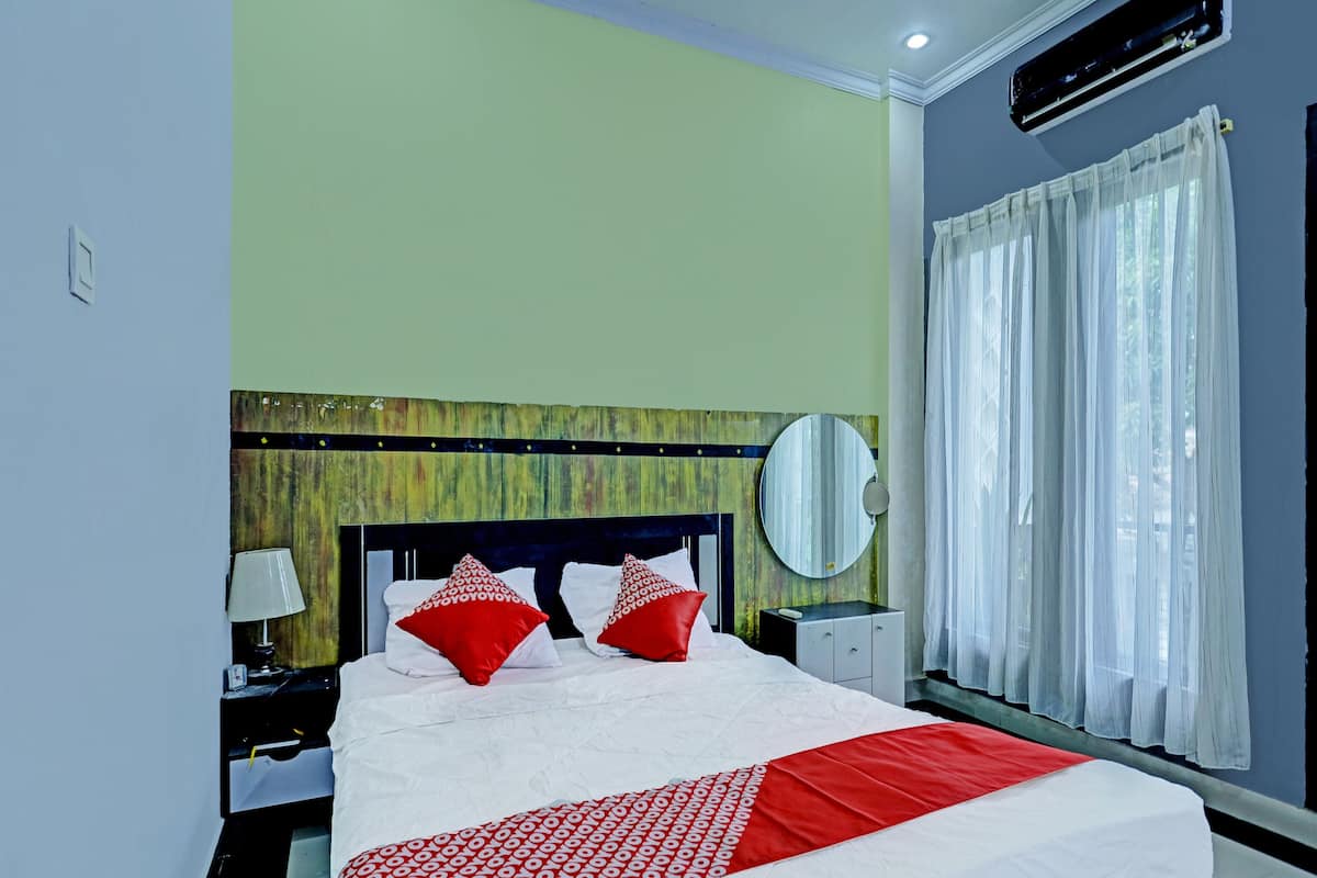 A hotel room with a bed, a nightstand, a lamp, a mirror, and a window with curtains.