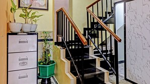A staircase with black railings and wooden handrails, leading to a landing with a green plant pot and a filing cabinet with drawers. - Hotel O Lia Stay Syariah (Batam)