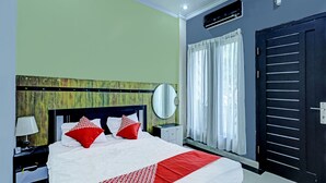 A hotel room with a bed, a nightstand, a mirror, a window with curtains, and a door. - Hotel O Lia Stay Syariah (Batam)