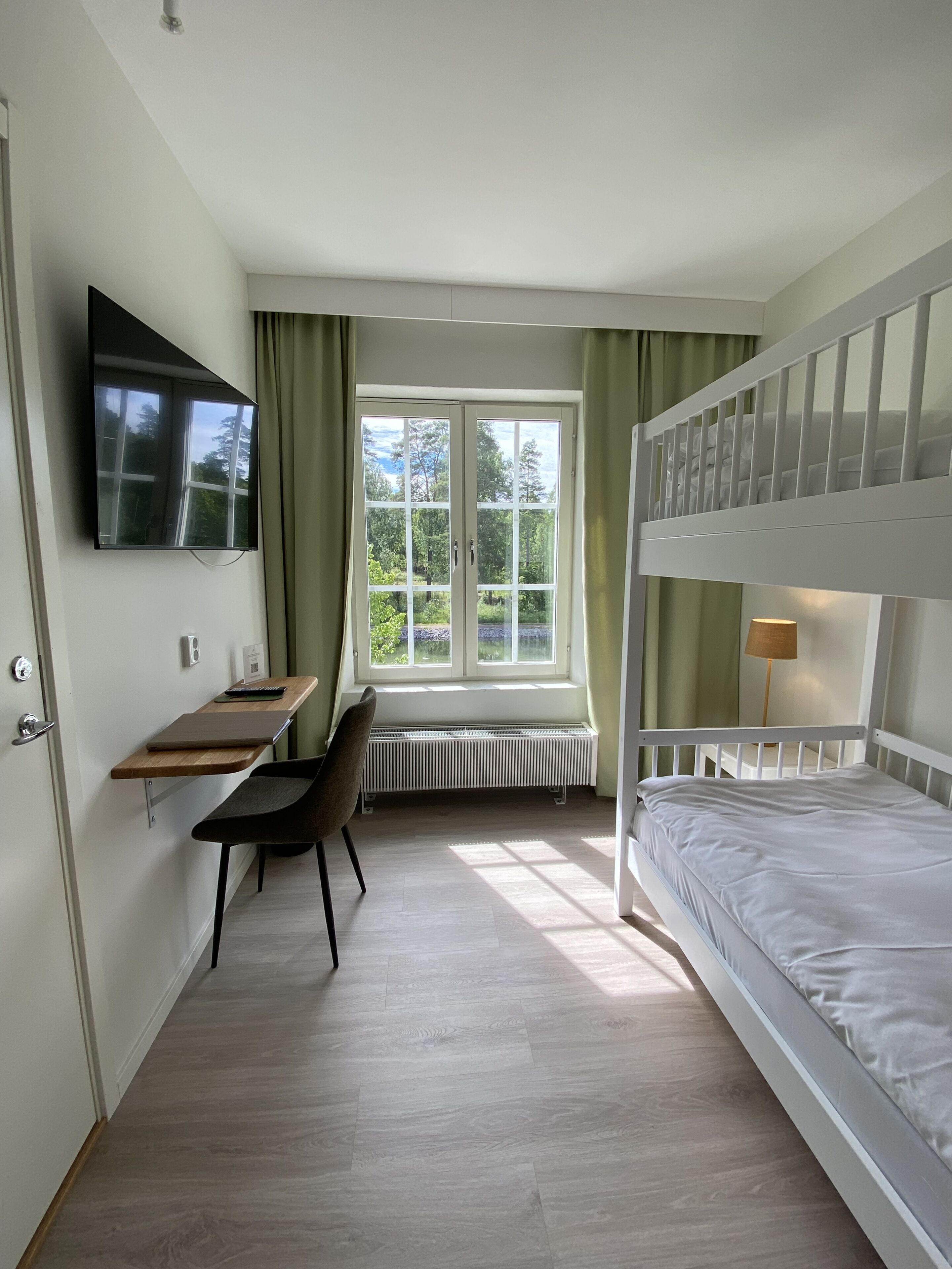 Ein Schlafzimmer mit Etagenbett, Schreibtisch mit Stuhl, Heizkörper und Wand-Fernseher.