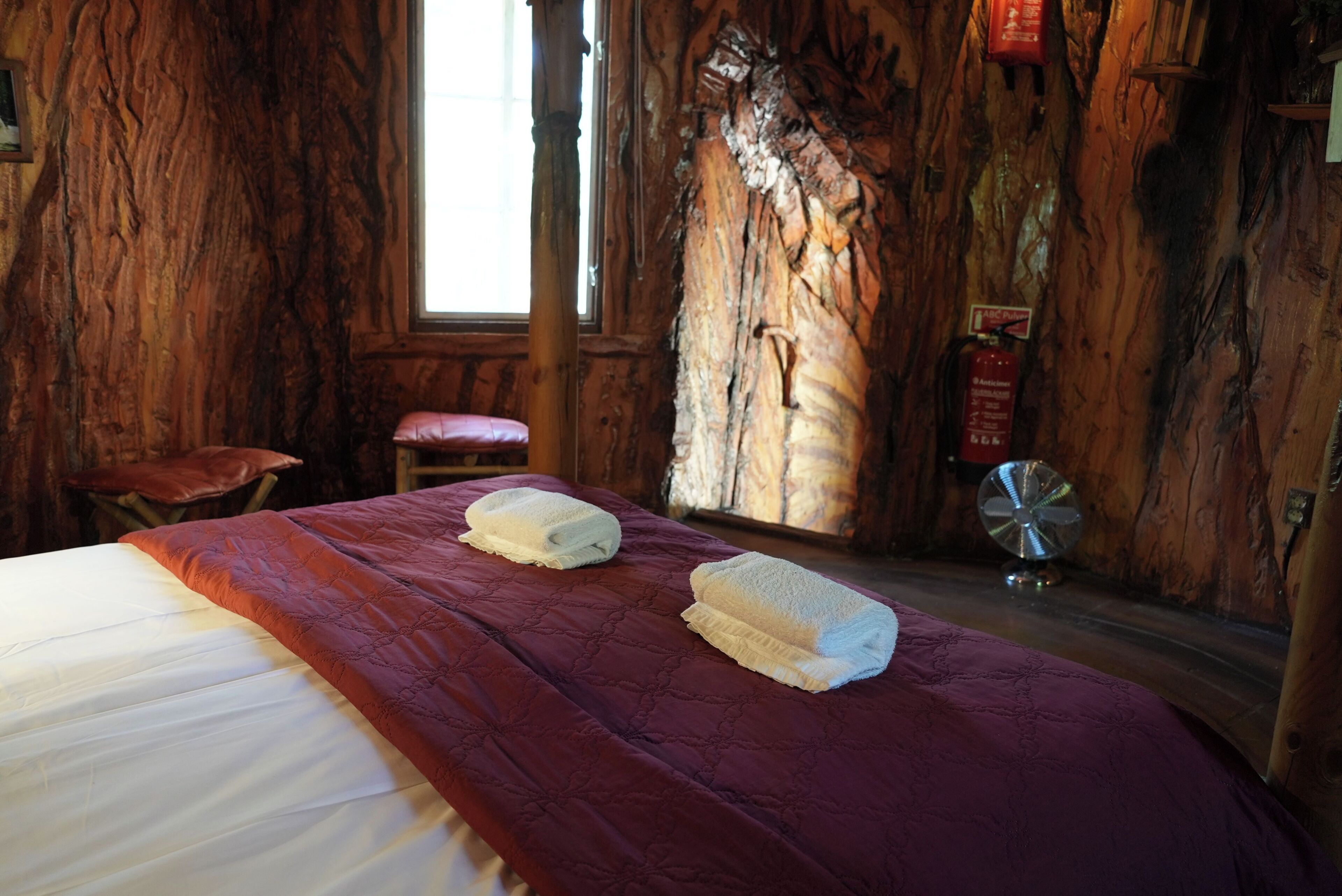 A wooden room with a bed, two towels, a red bench, and a fire extinguisher.