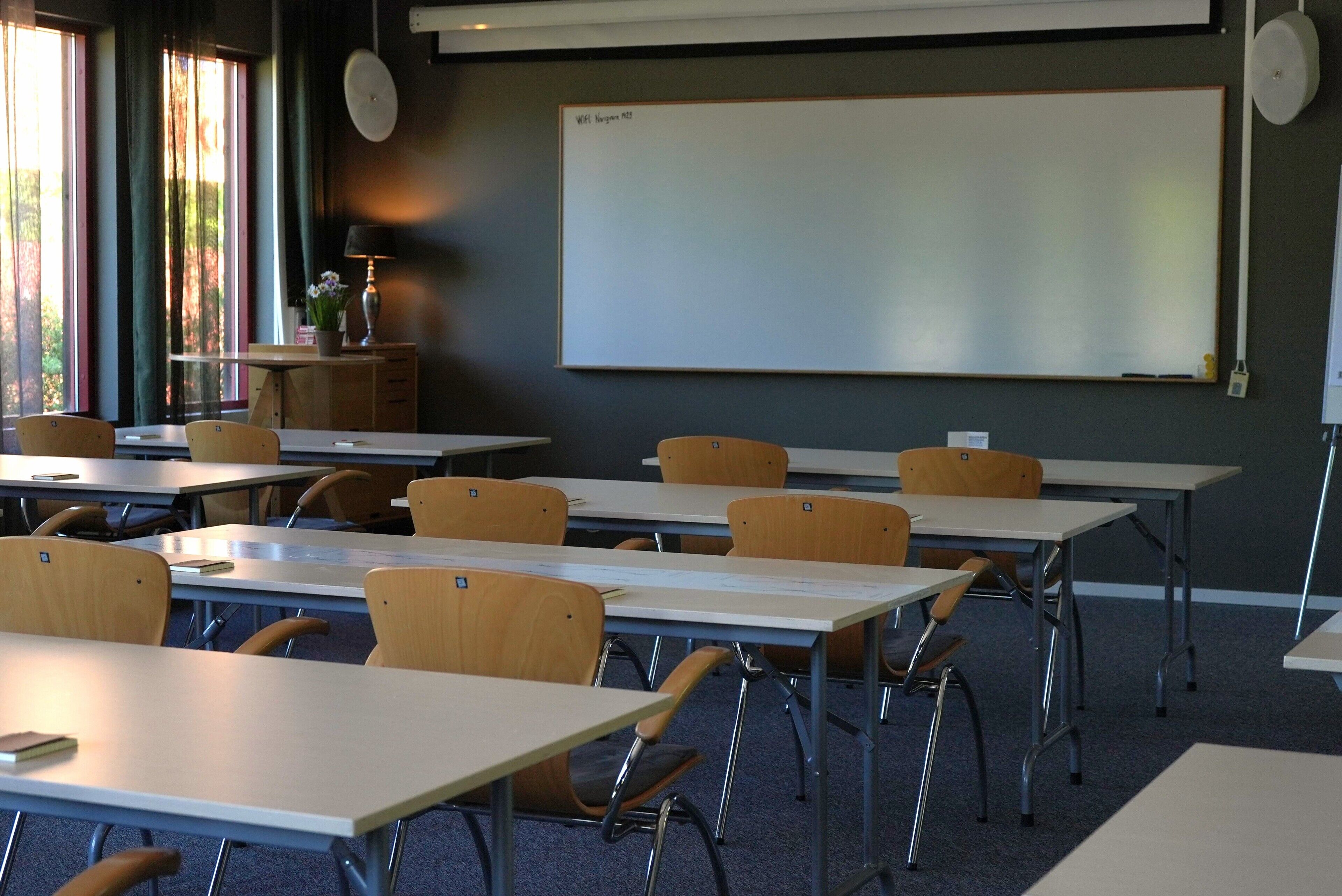 A classroom with desks, chairs, a whiteboard, and a window with curtains.