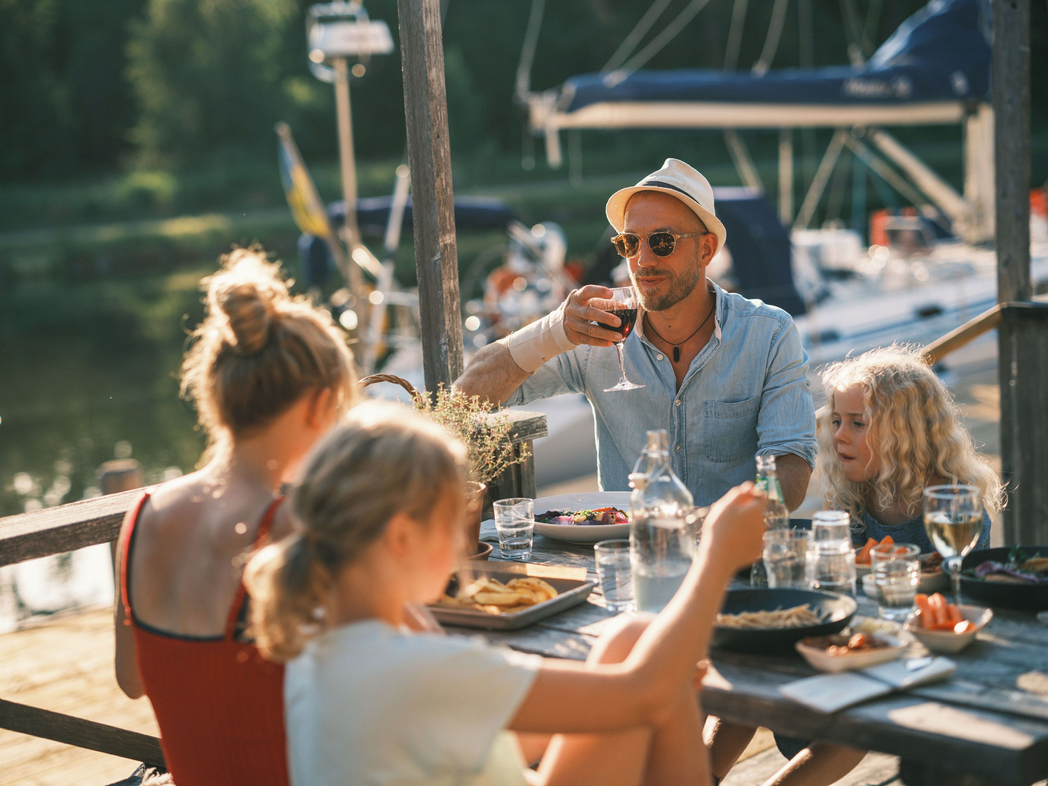 A dining table with food and drinks, a wooden deck, and a marina in the background.