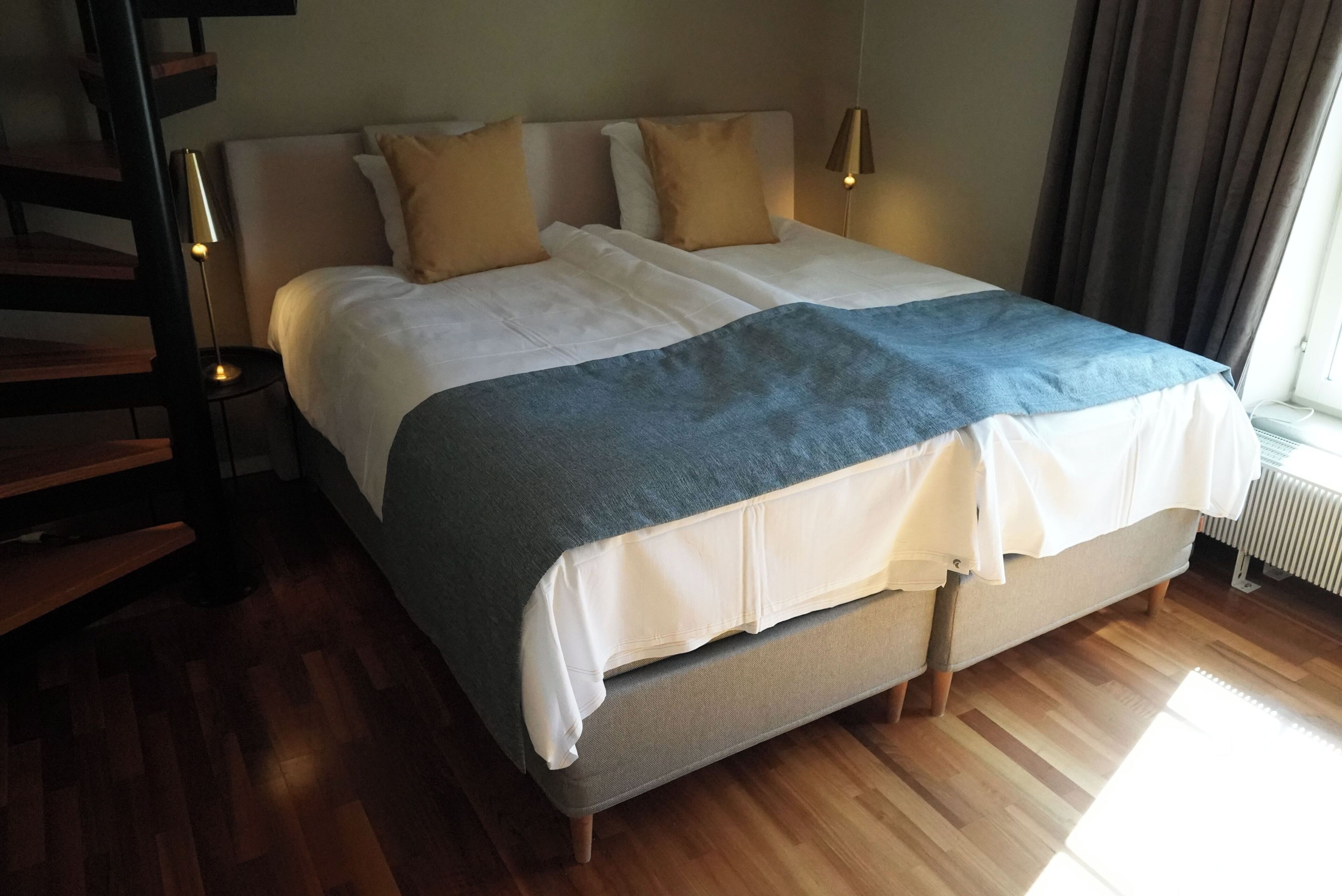 Una cama doble con una manta azul, dos almohadas y una lámpara de noche.