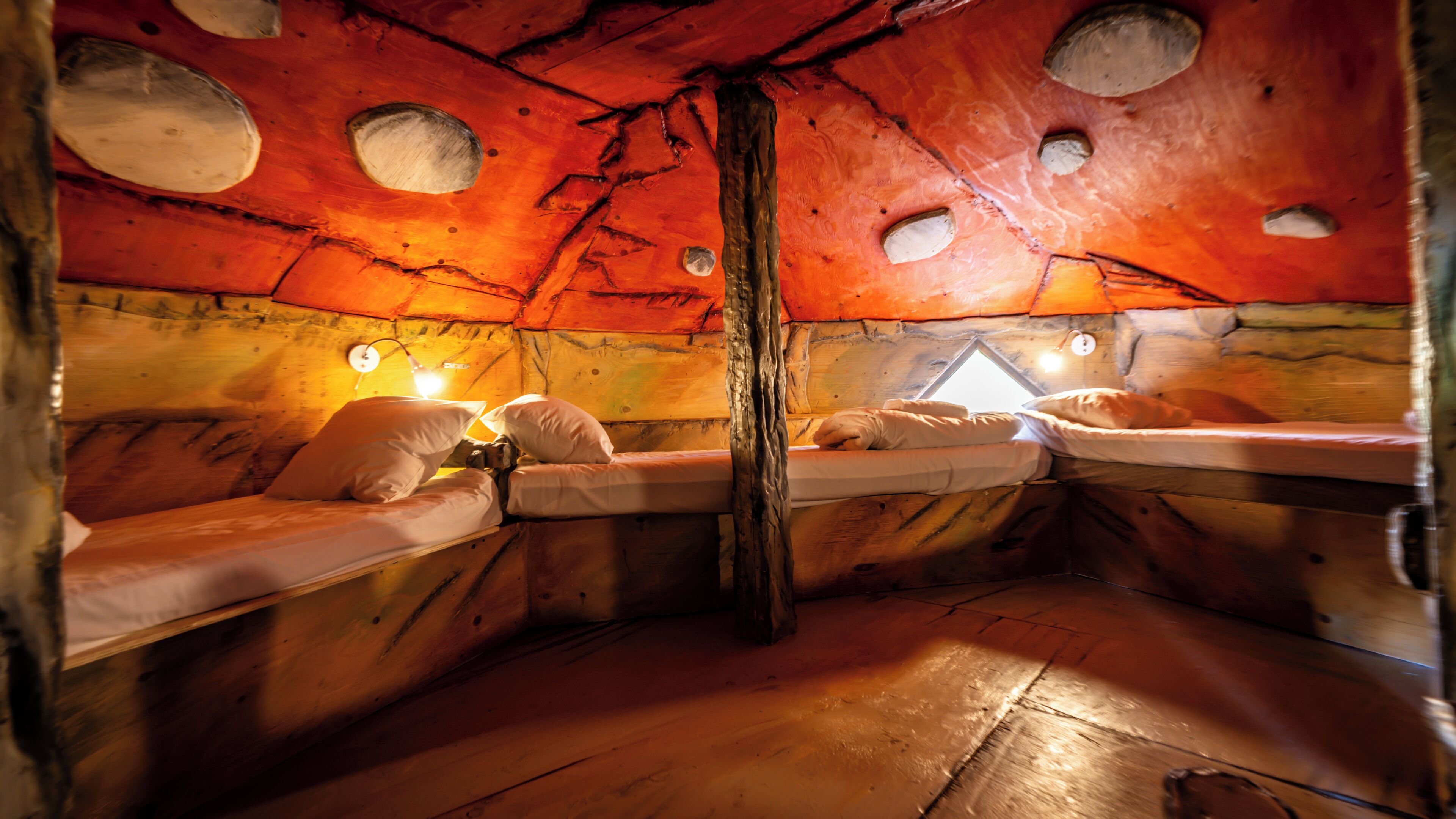 A cabin with wooden walls, a central wooden pillar, and two beds with pillows.