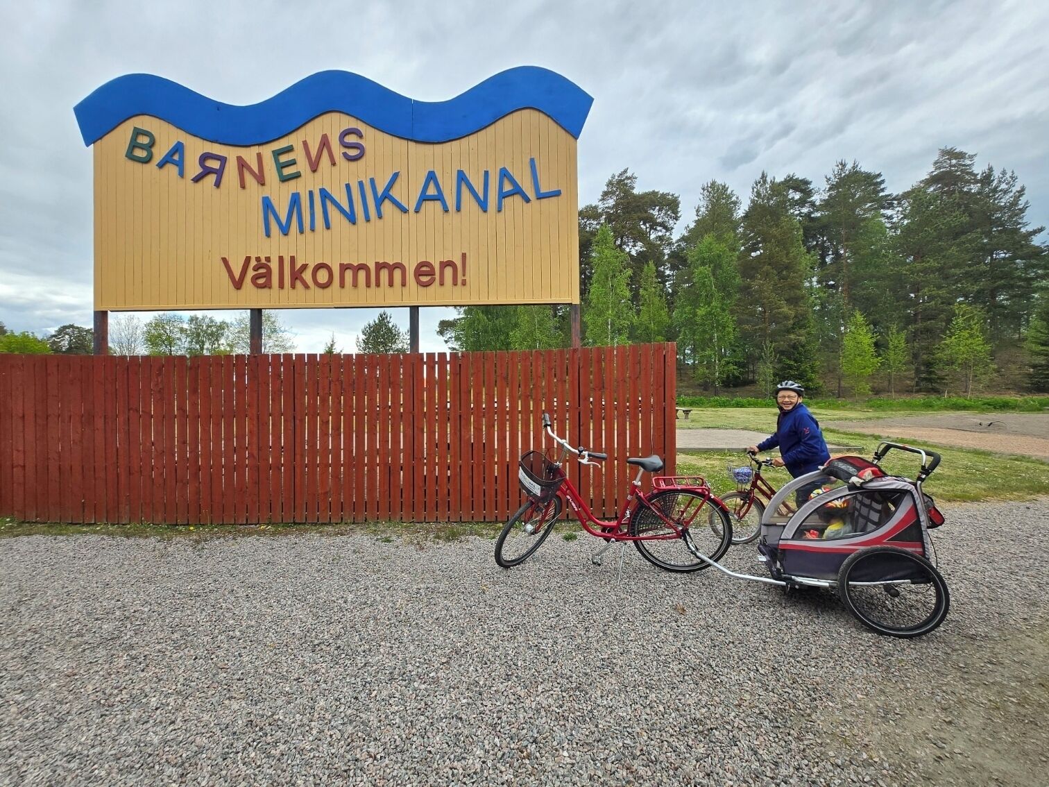 Un letrero de madera con el texto 'Barnevs Minikanal' y '¡Bienvenidos!' señalando una entrada acogedora.