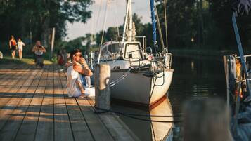 A wooden dock with a sailboat moored at a pier, surrounded by calm water and trees.