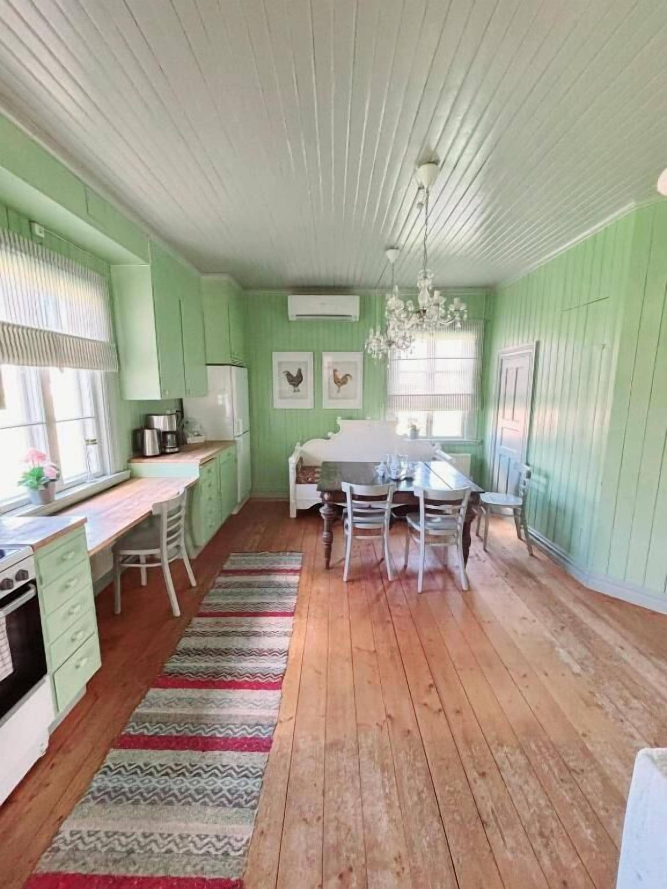 Une cuisine avec un coin repas, un plancher en bois, des murs verts et un lustre.