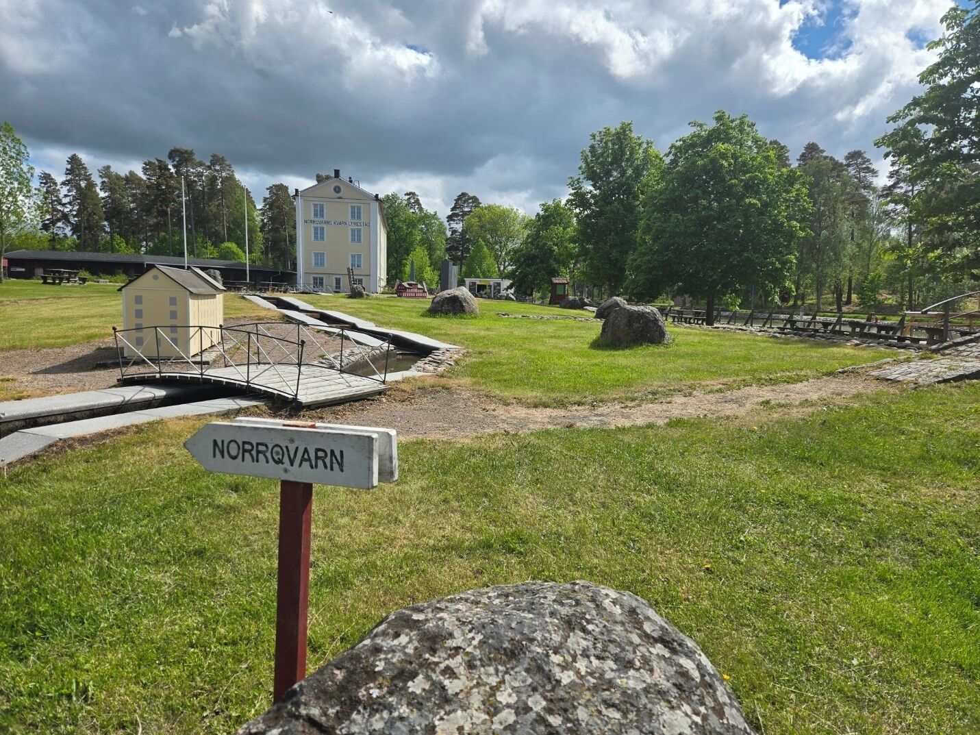 Un parc avec un pont, un panneau indiquant « NORROVARN », et un bâtiment en arrière-plan.
