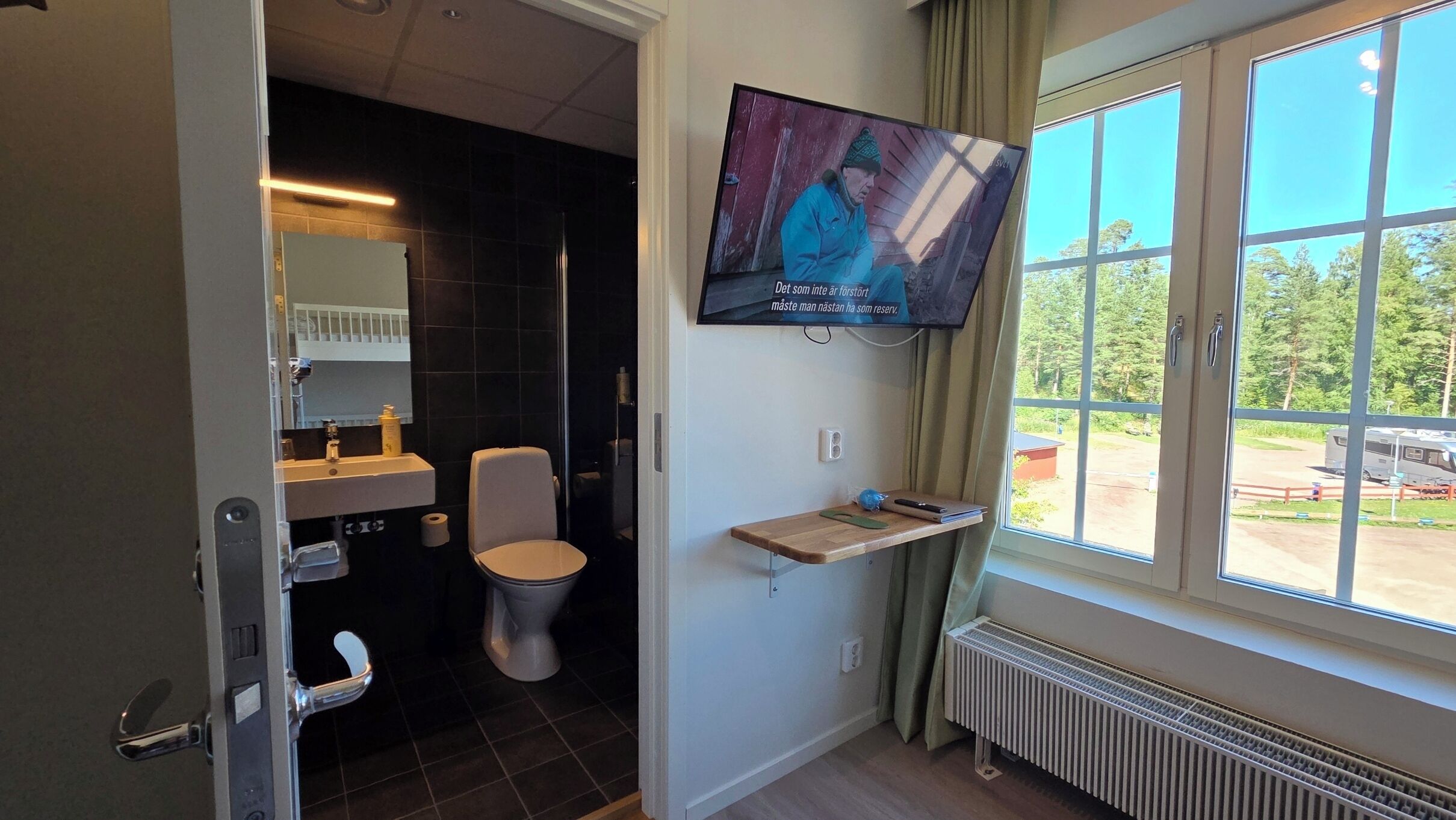 Un baño moderno con inodoro, lavamanos y televisor montado.
