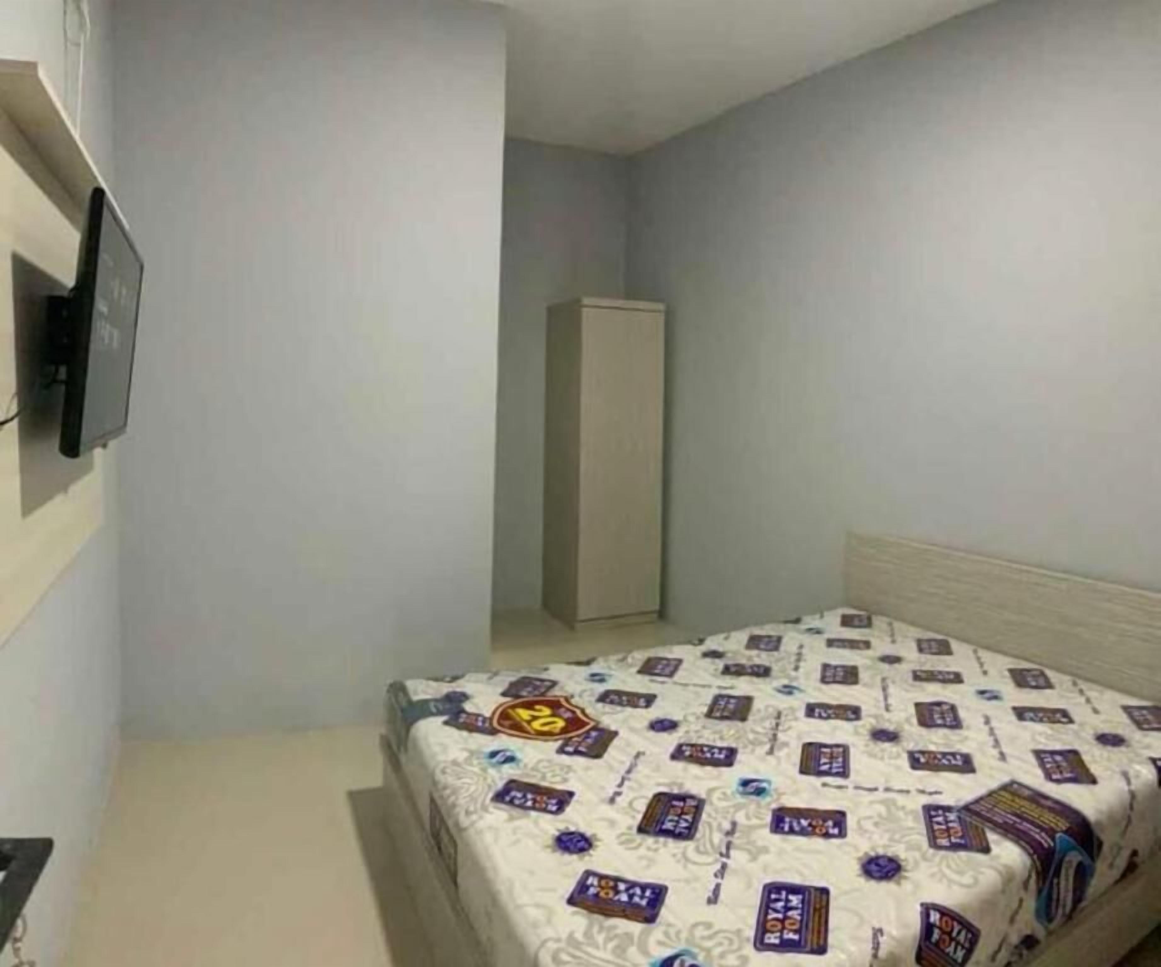 Ein kleiner, schlicht eingerichteter Raum mit einem Bett, einem Kleiderschrank und einem Fernseher an der Wand.