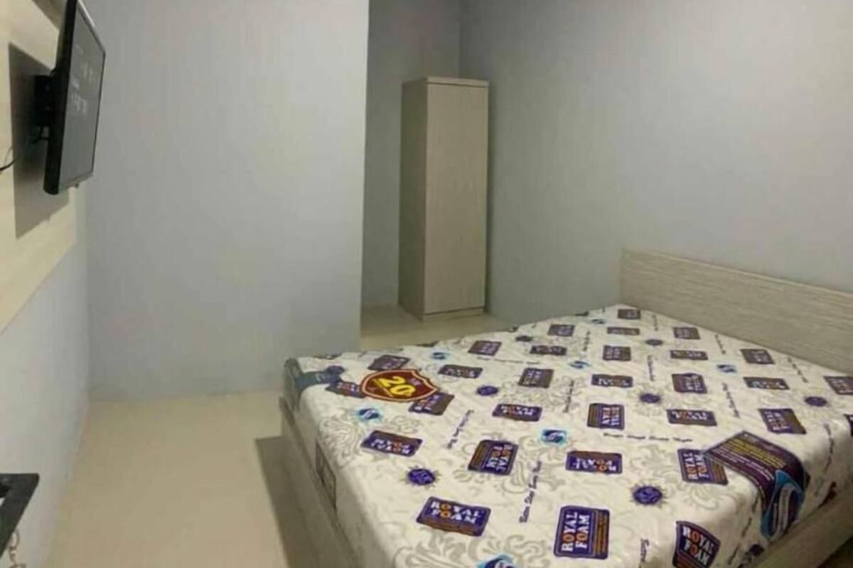 A small, sparsely furnished room with a bed, a wardrobe, and a television on the wall.