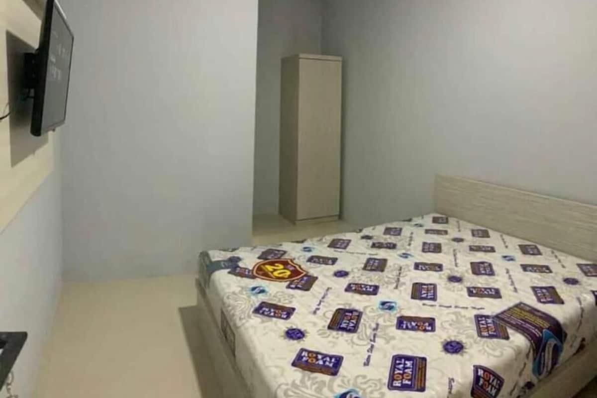 A small, sparsely furnished room with a bed, a wardrobe, and a television on the wall.