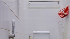 A small, clean bathroom with white tiles, a white toilet, a red waste basket, and a visible pipe. - Hotel O Ringin Pitu 1 Syariah (Batam)
