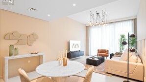 A modern living room with a round marble table, beige sofas, and a television. - Aya - Outstanding 1BR Apartment With Amazing Creek Views (Dubai)